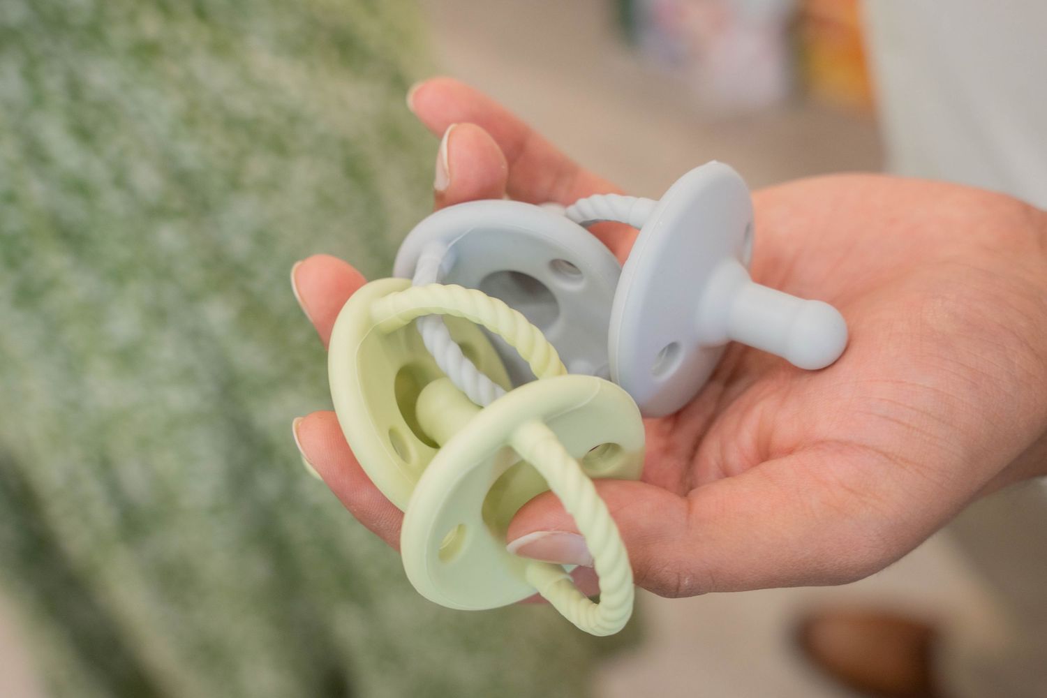 Close-up of a hand holding three pastel green and blue baby pacifiers as a baby shower favor or game prize.