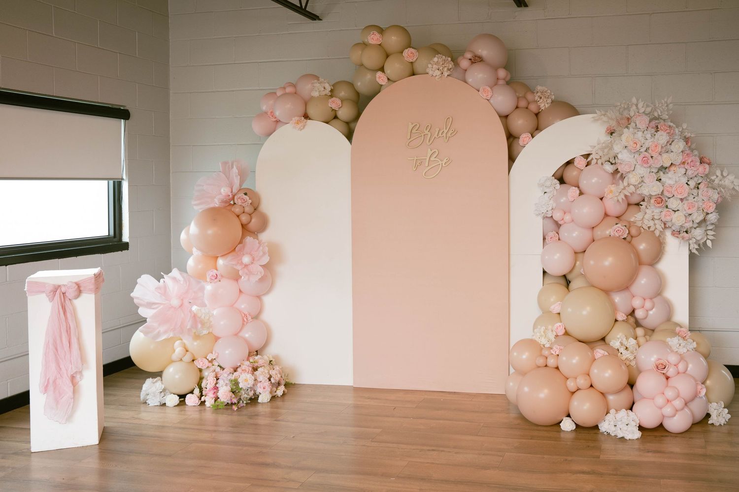 Pink and peach balloon garland with arched backdrop panels and floral arrangements decorating a bridal shower venue.