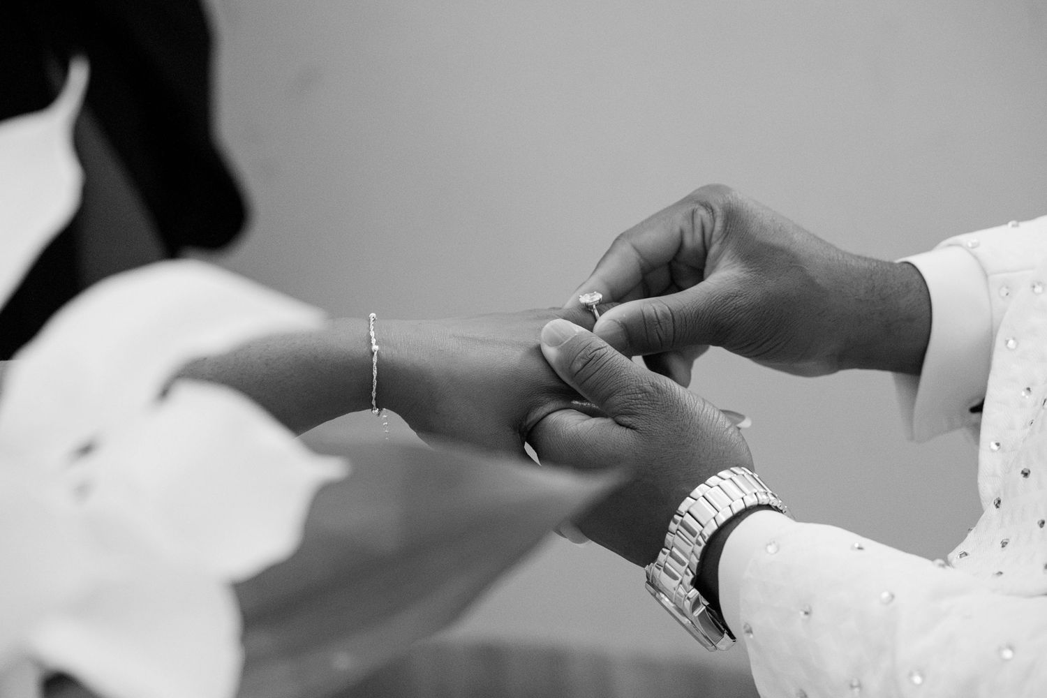 Black and white close-up of a groom placing a wedding ring on the bride's finger during the ceremony.