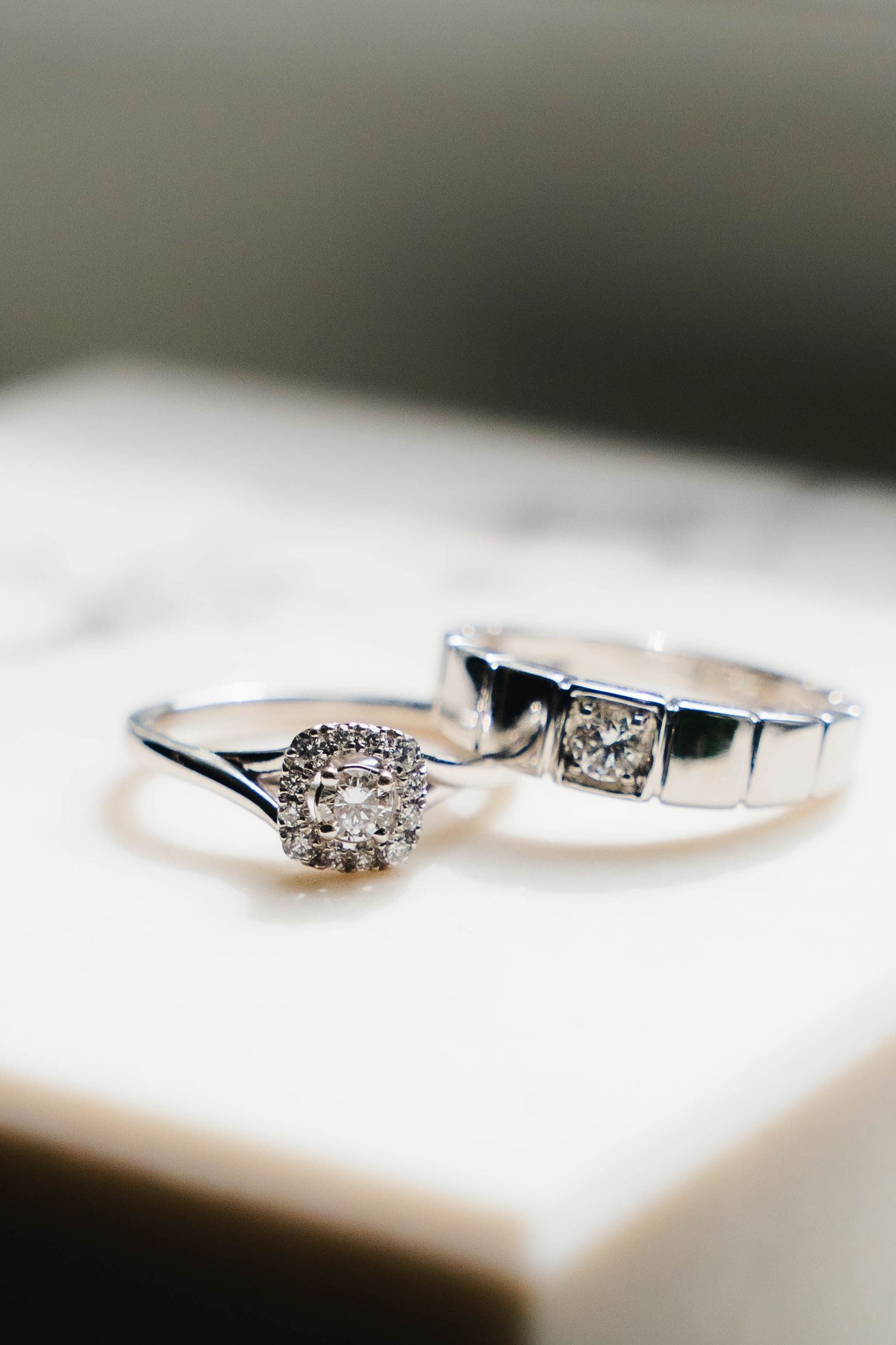Halo diamond engagement ring and men's square-cut diamond wedding band resting together on a white marble surface.