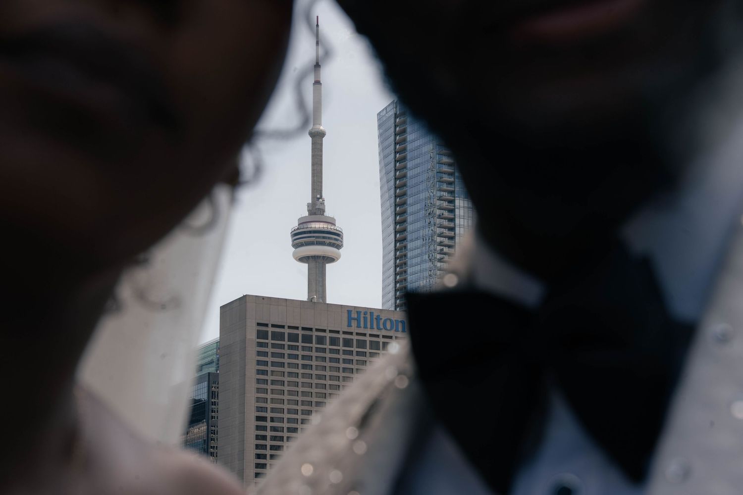 The CN Tower and a Hilton hotel are framed between the blurred silhouettes of a bride and groom in a Toronto wedding photo.
