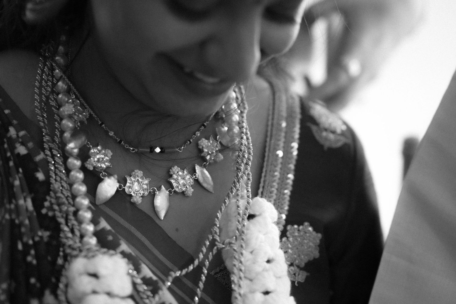 Black and white close-up of a bride wearing ornate floral jewelry and a white flower garland, smiling softly during her wedding.
