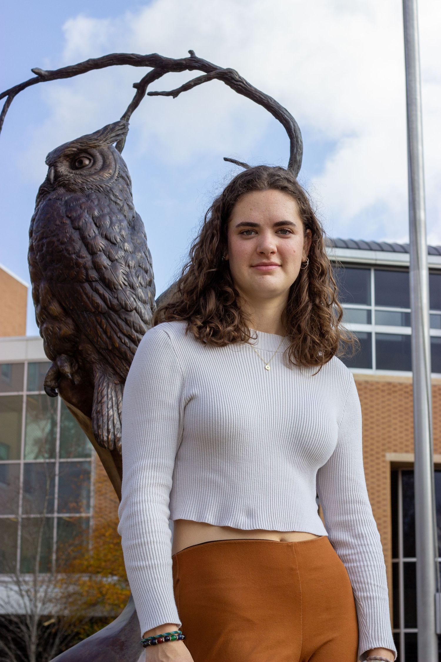 Young woman poses before bronze owl sculpture outside university building in autumn.