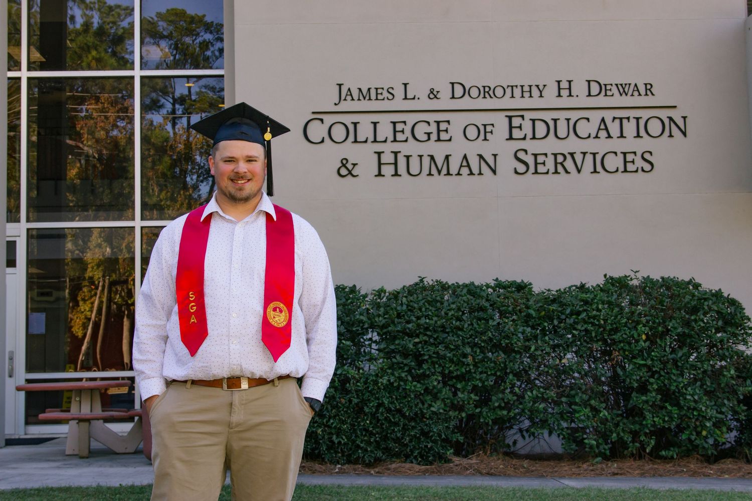 Graduate posing before James L. and Dorothy H. Dewar College of Education and Human Services sign.