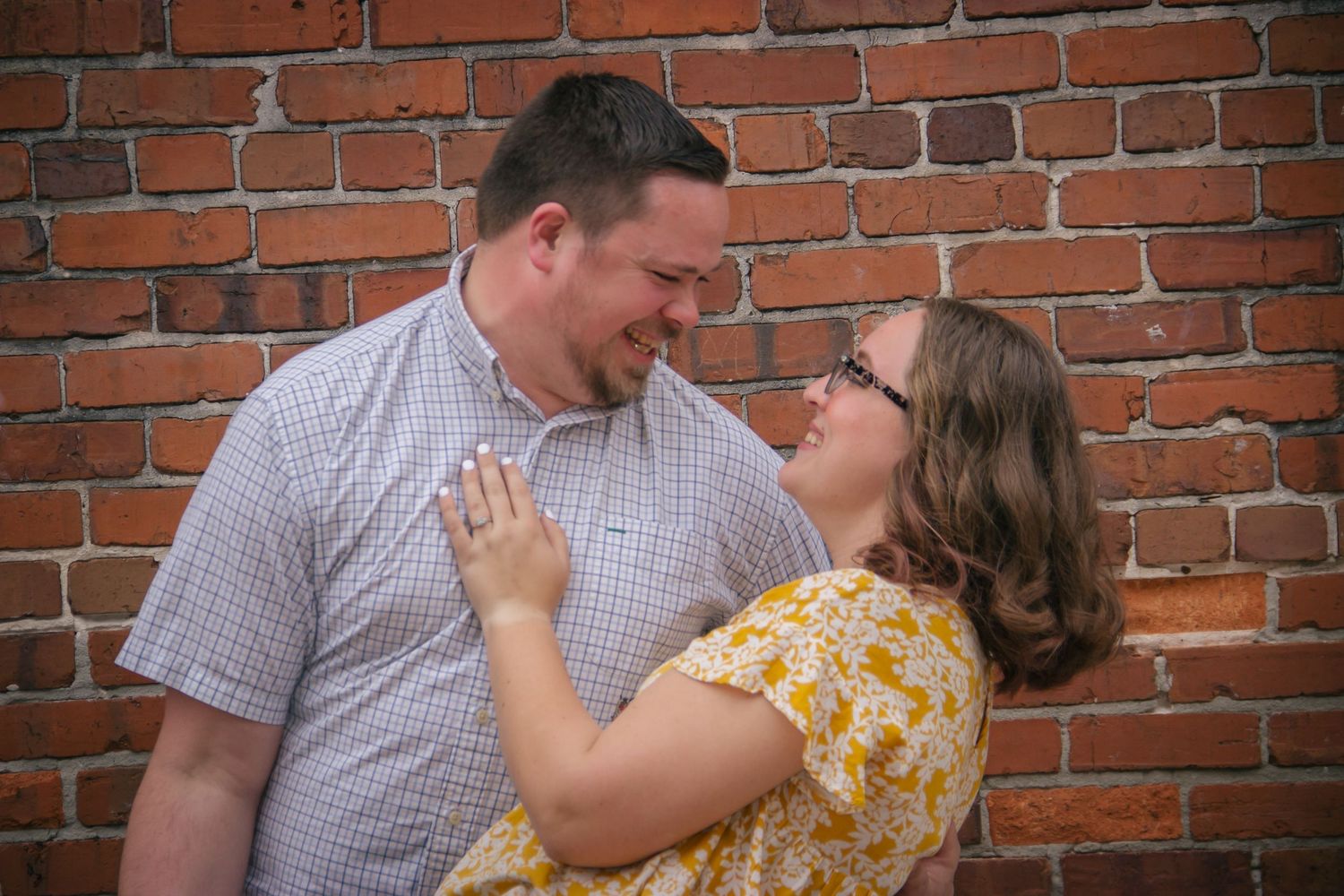 Engaged couple gazing at each other lovingly against rustic red brick wall outdoors.