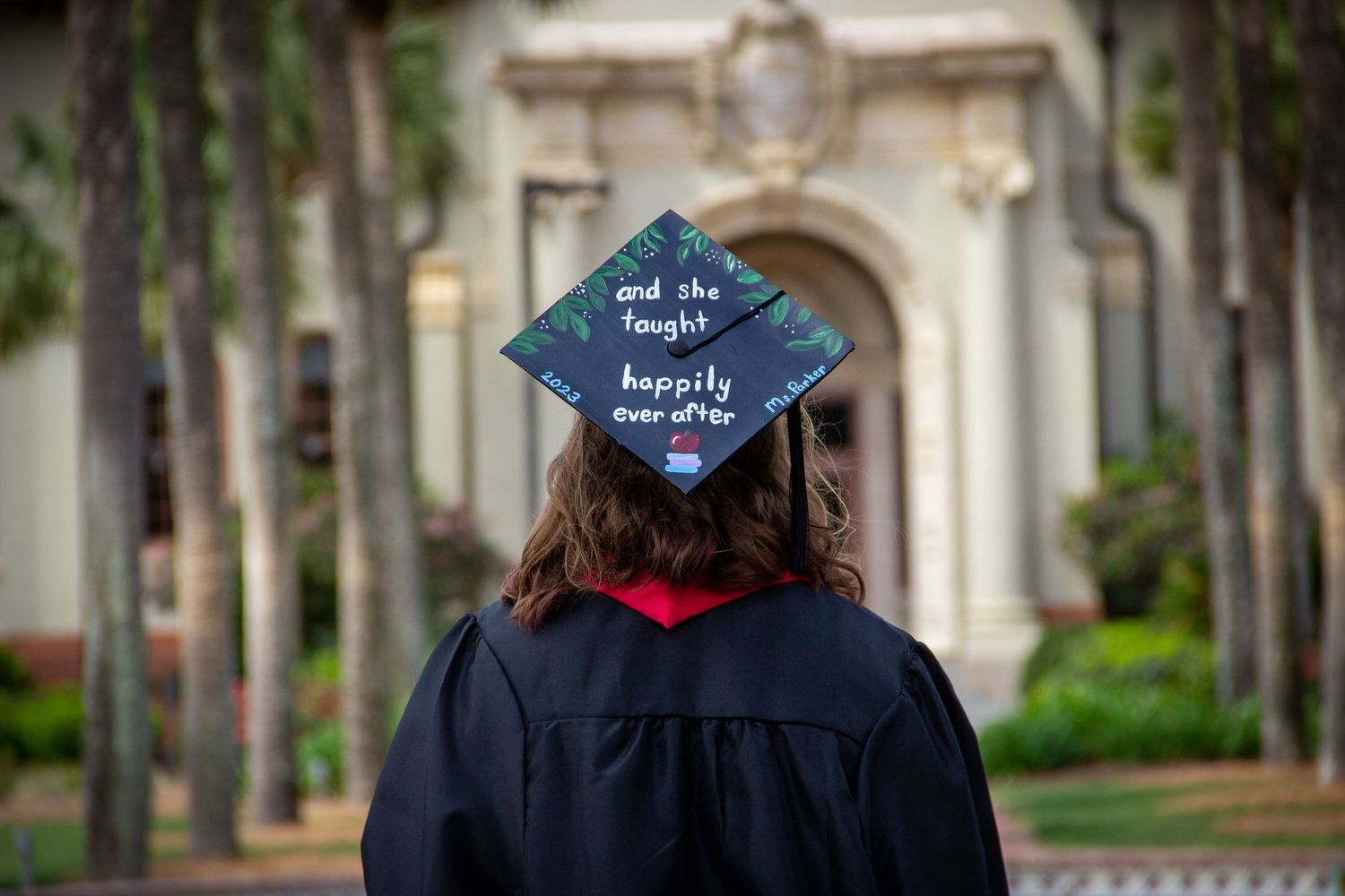 Close back view of decorated graduation cap reading and she lived happily ever after outdoors.