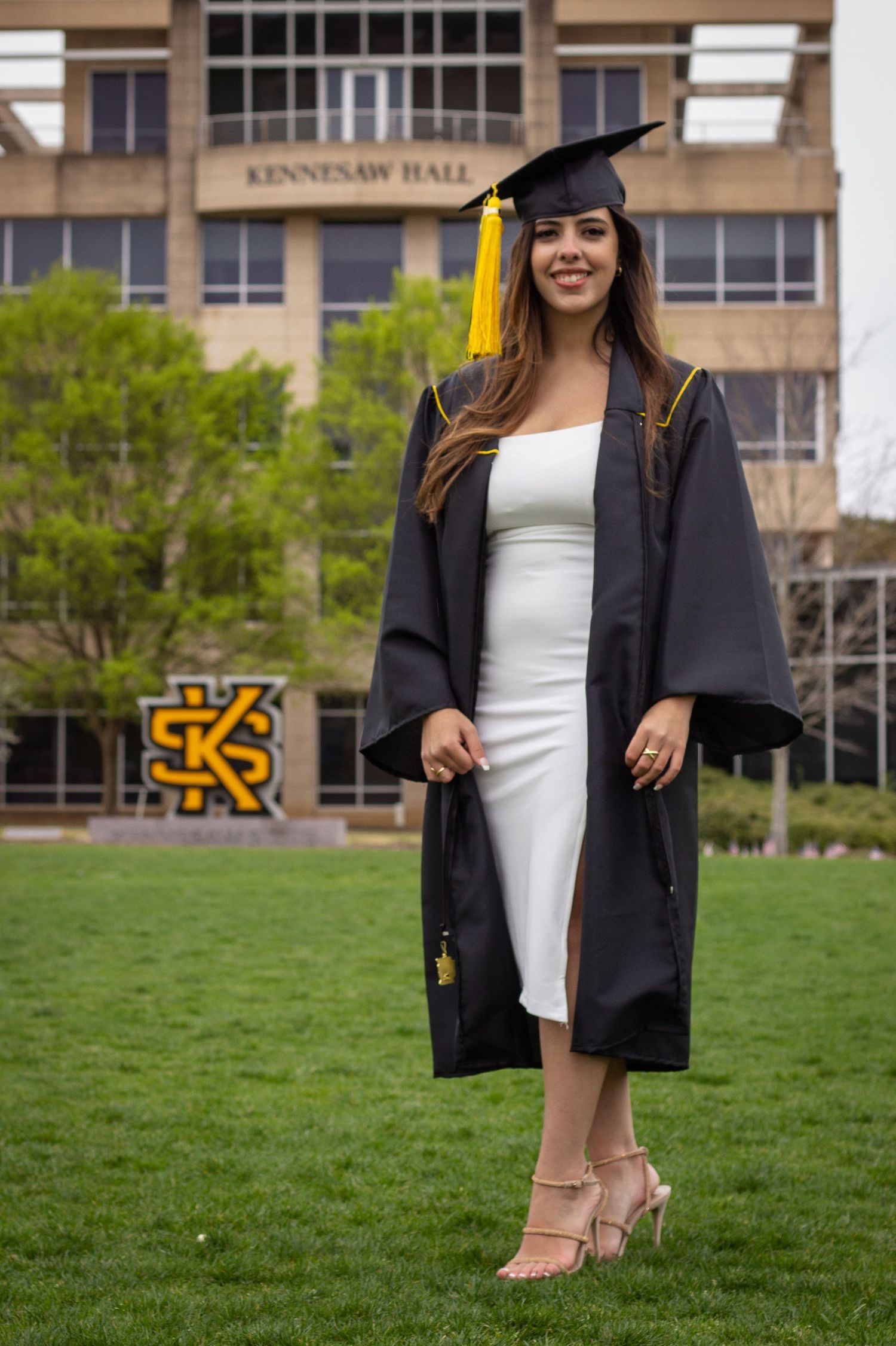 Female graduate in black cap and gown with white dress posing at Kennesaw State University.