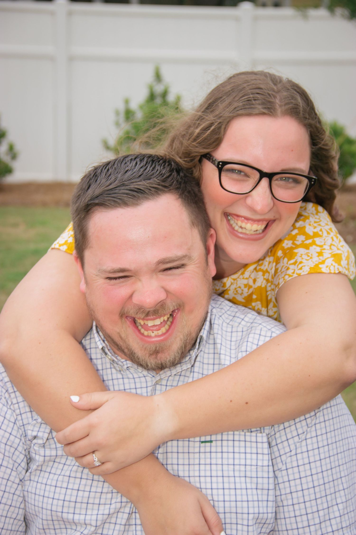 Laughing couple in close embrace outdoors, woman with glasses wrapping arms around smiling man.