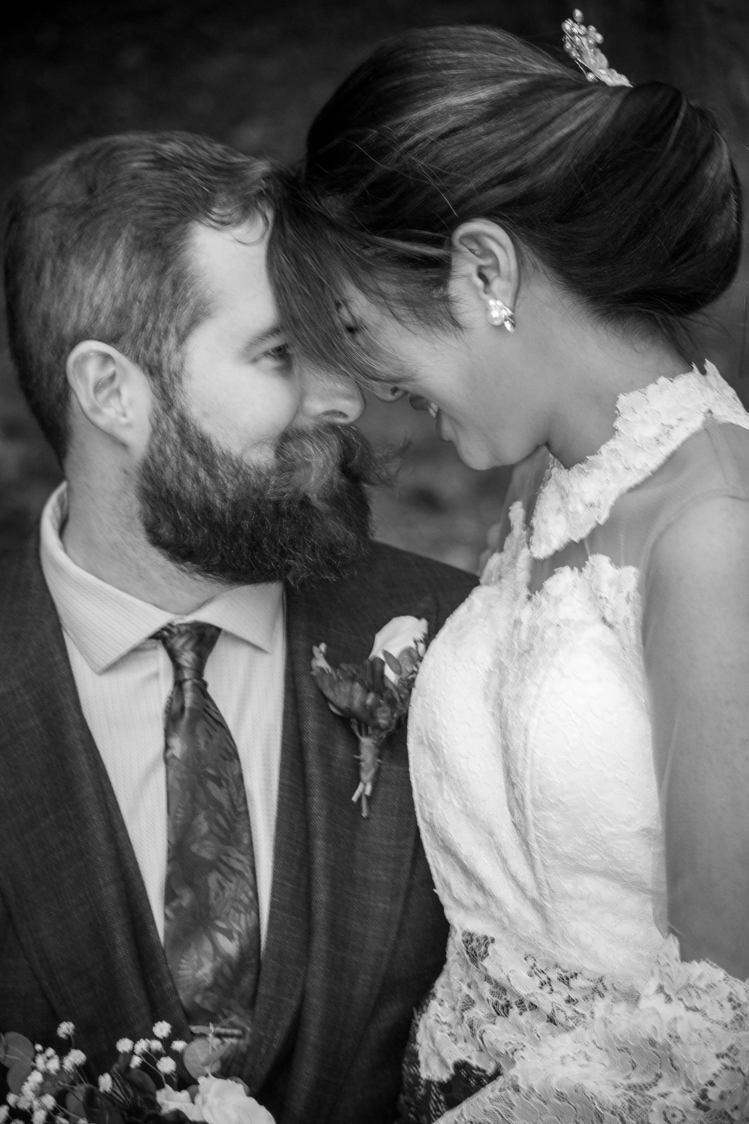 Black and white intimate portrait of bearded groom and smiling bride touching foreheads together.