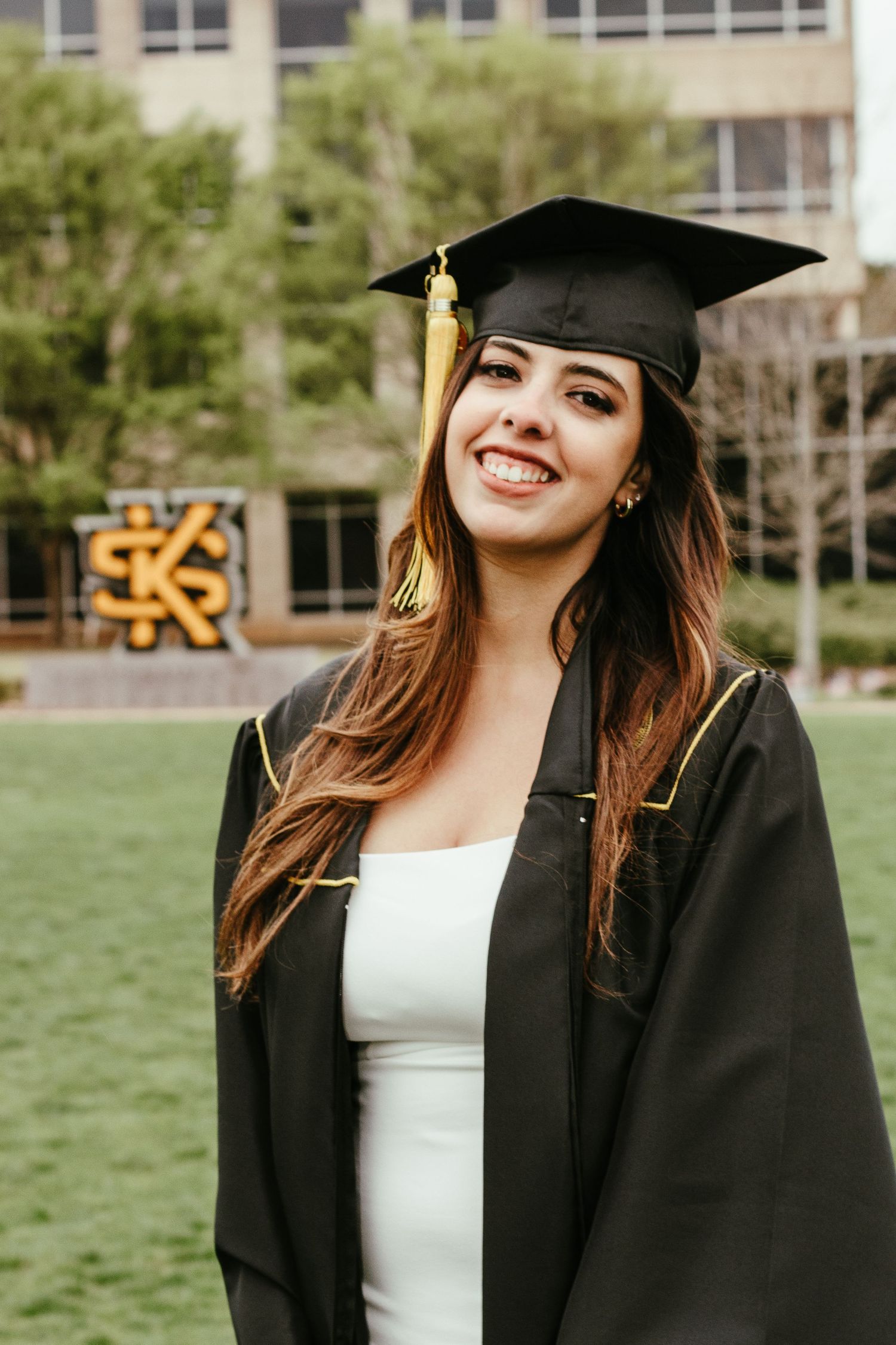 Smiling female graduate in black cap and gown with gold tassel at Kennesaw State University campus.