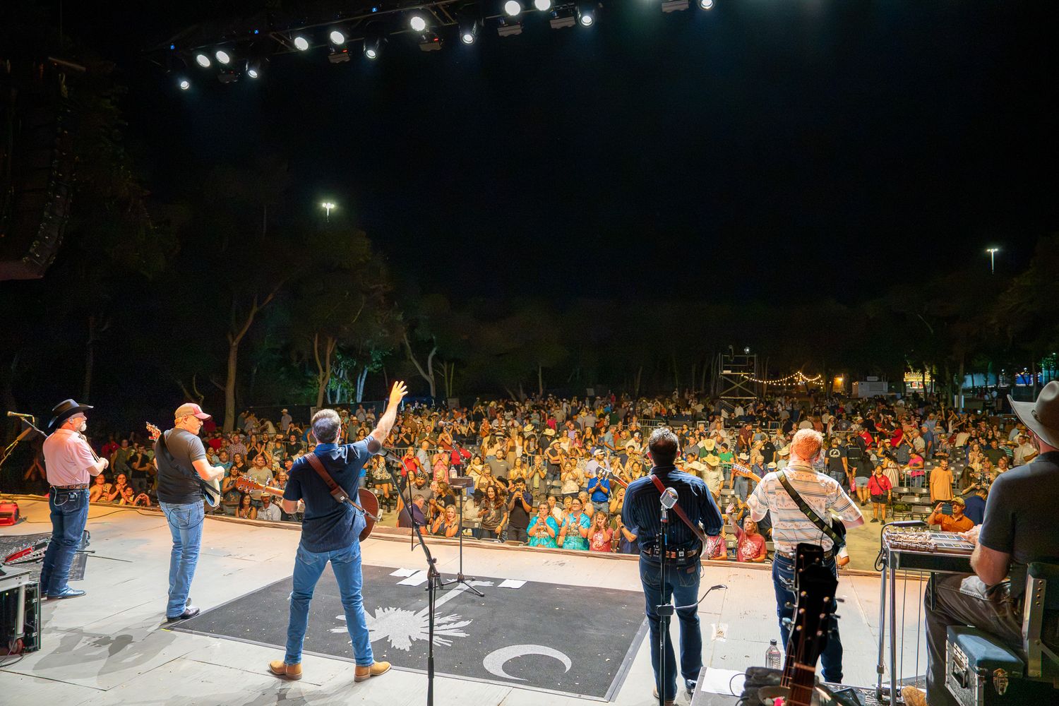 A live band performs on an outdoor stage at night before a large crowd at a music festival.