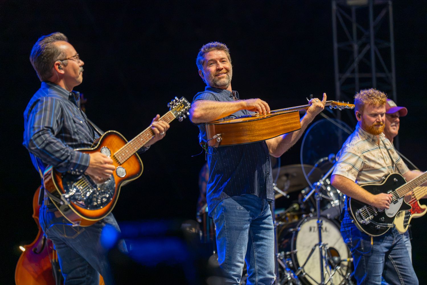 Three musicians performing on stage, playing guitar and dulcimer under bright concert lights.