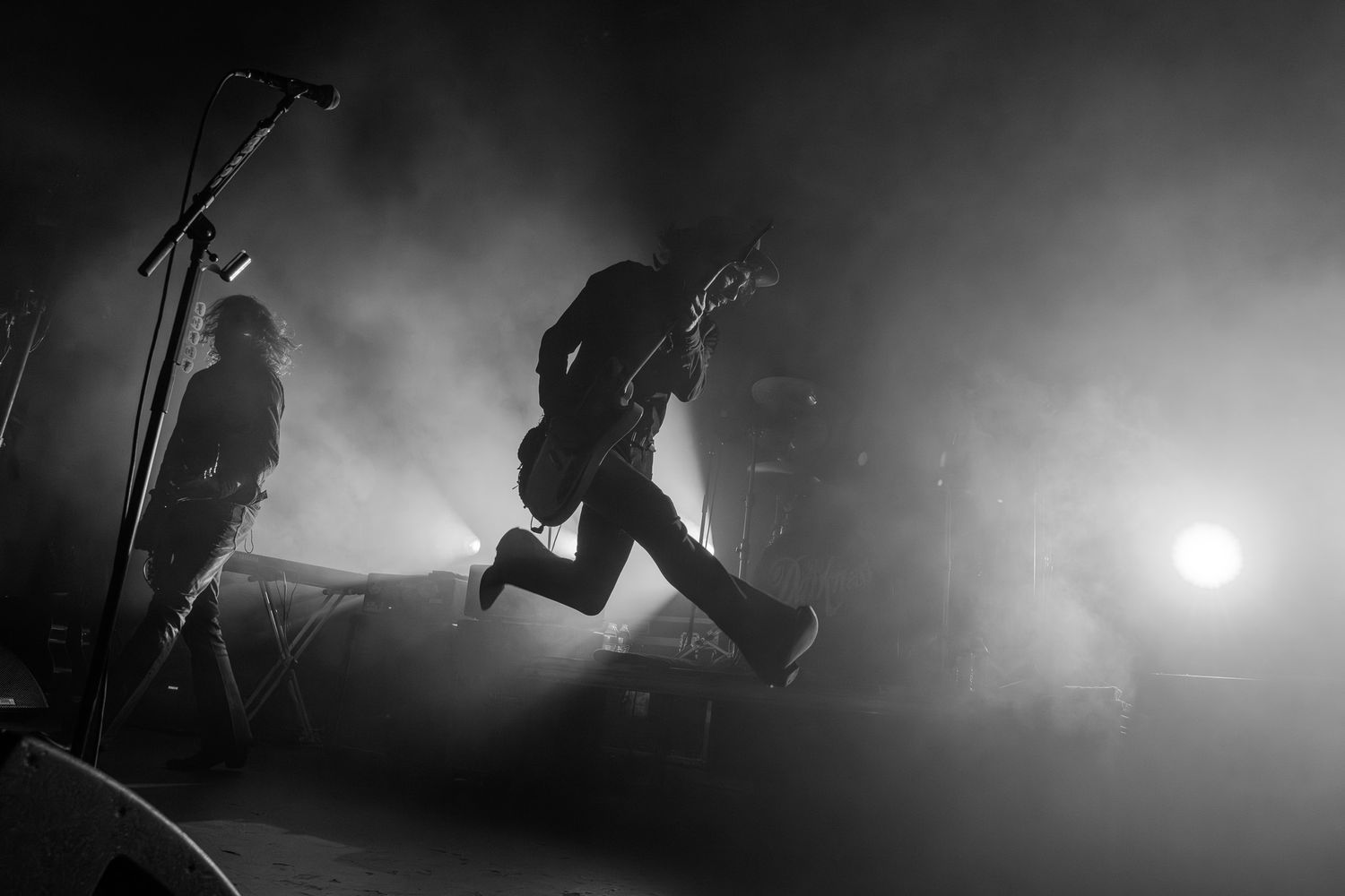 Justin Hawkins in a Black-and-white photo of The Darkness performing on a smoky, dramatically backlit concert stage at Emo's Austin.
