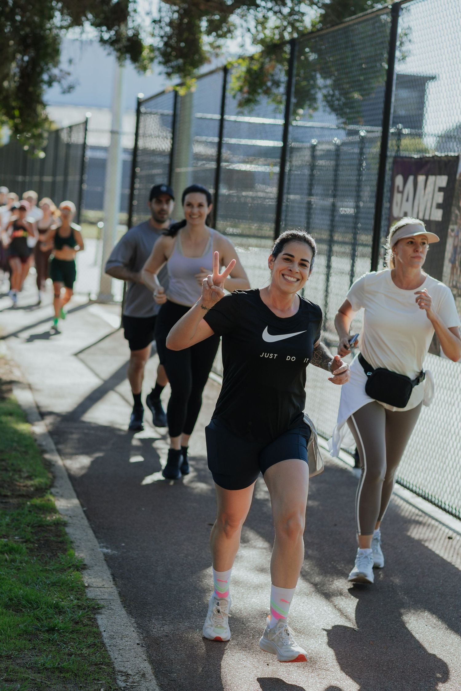 Smiling woman in Nike gear giving a peace sign while running with a group outdoors.
