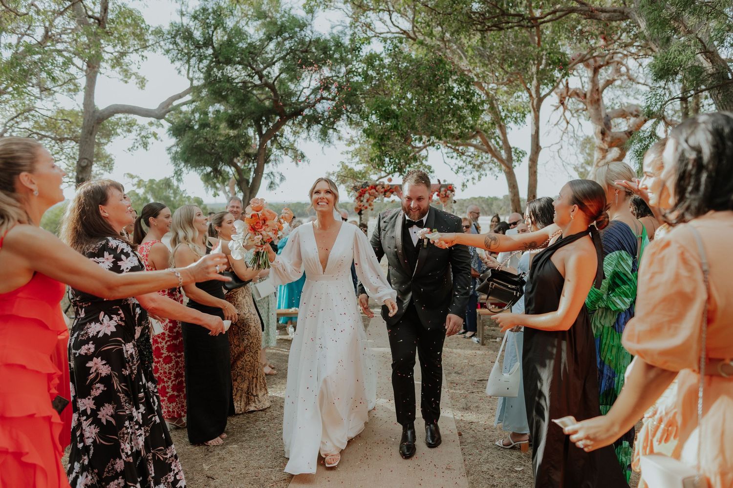Bride and groom walk through cheering guests in outdoor wedding ceremony exit.