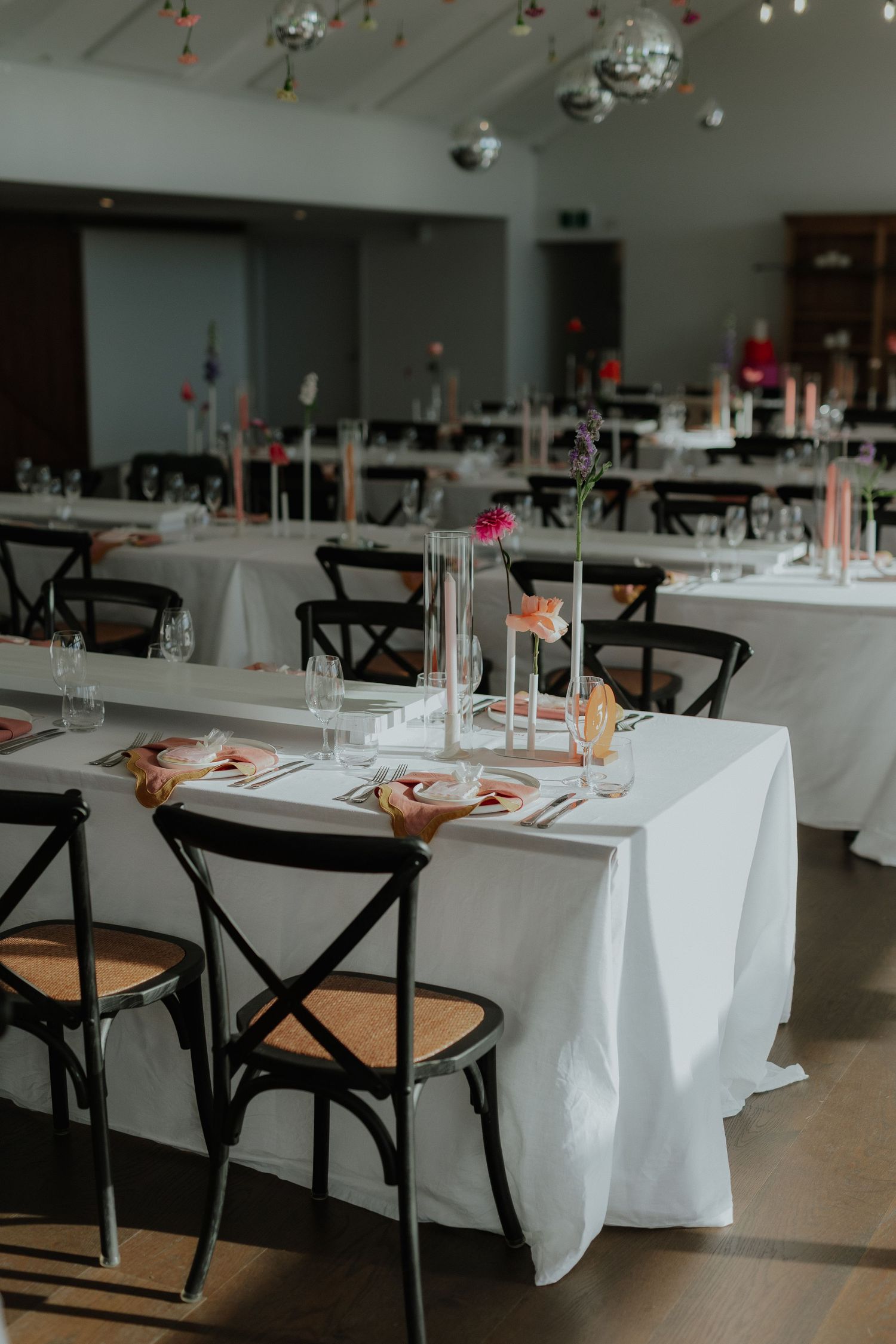 Modern wedding reception venue with white linen tables, black cross-back chairs and disco ball ceiling.