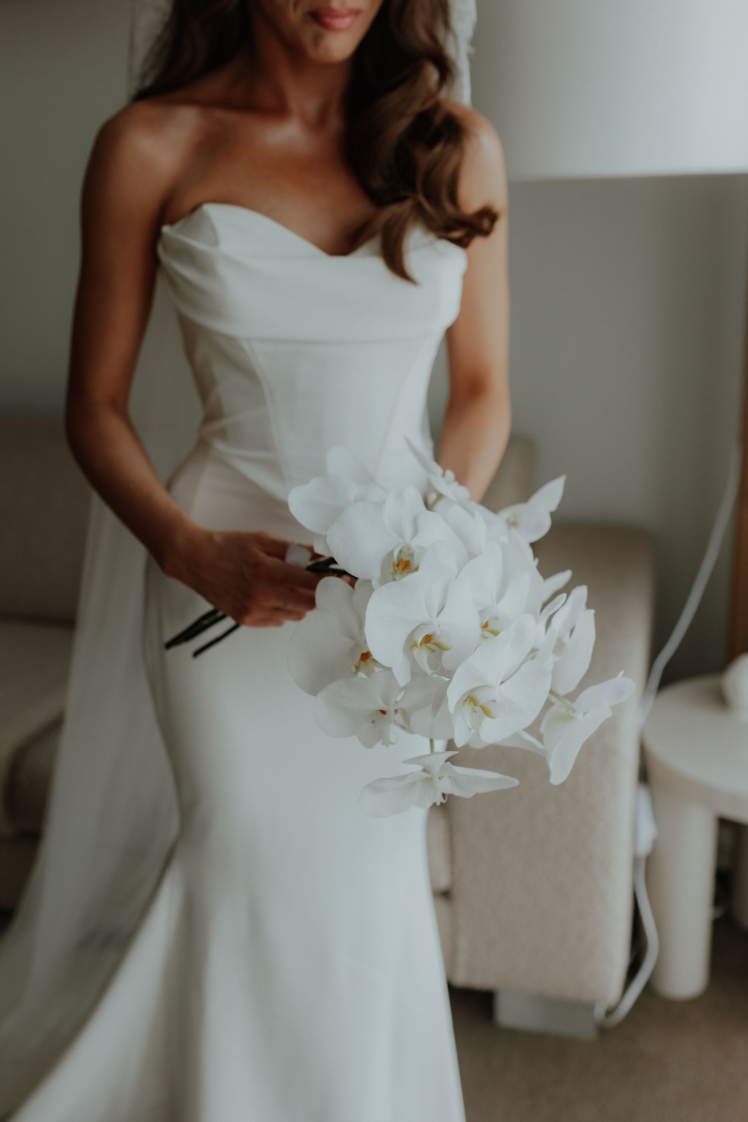 Bride in strapless white mermaid gown holding a minimalist white orchid bridal bouquet.