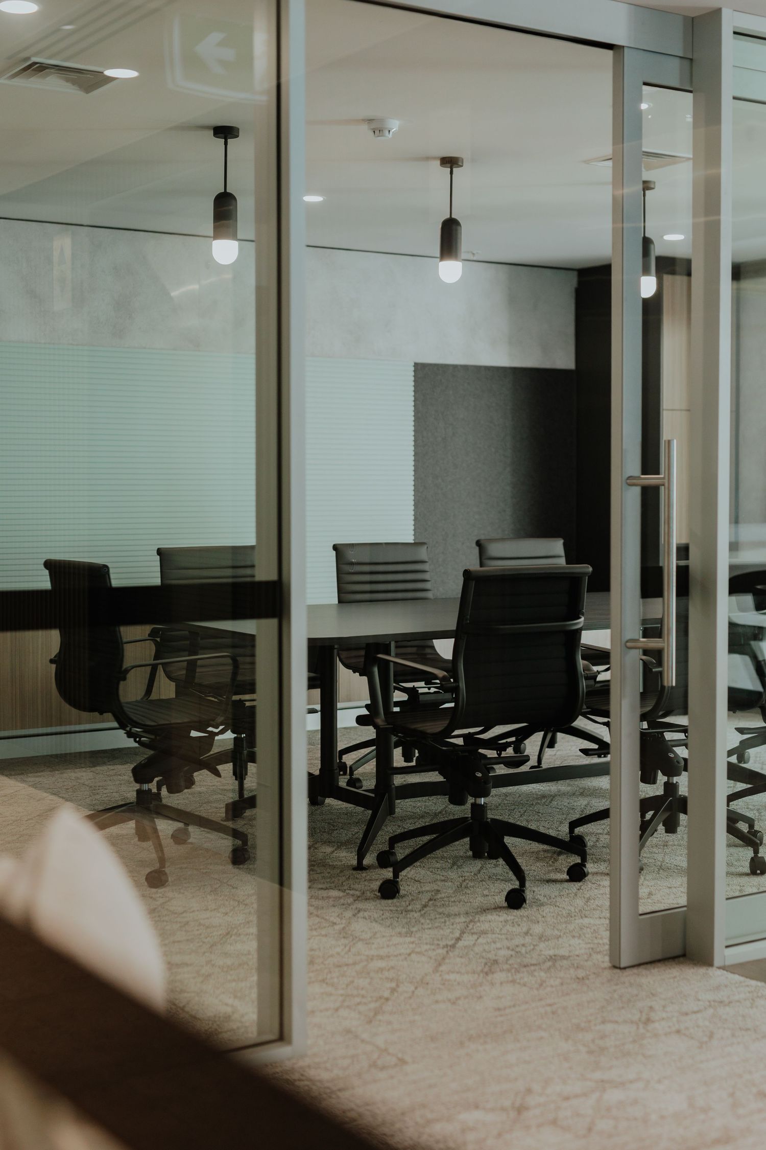 Modern glass-walled meeting room with black office chairs and pendant lighting fixtures.
