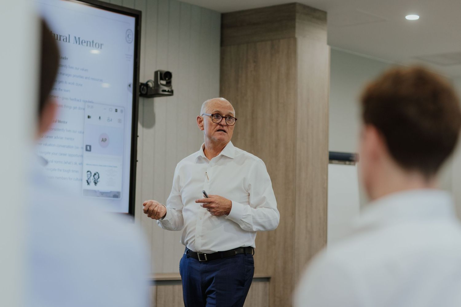 Senior male presenter in white shirt delivers a business presentation in a modern conference room.