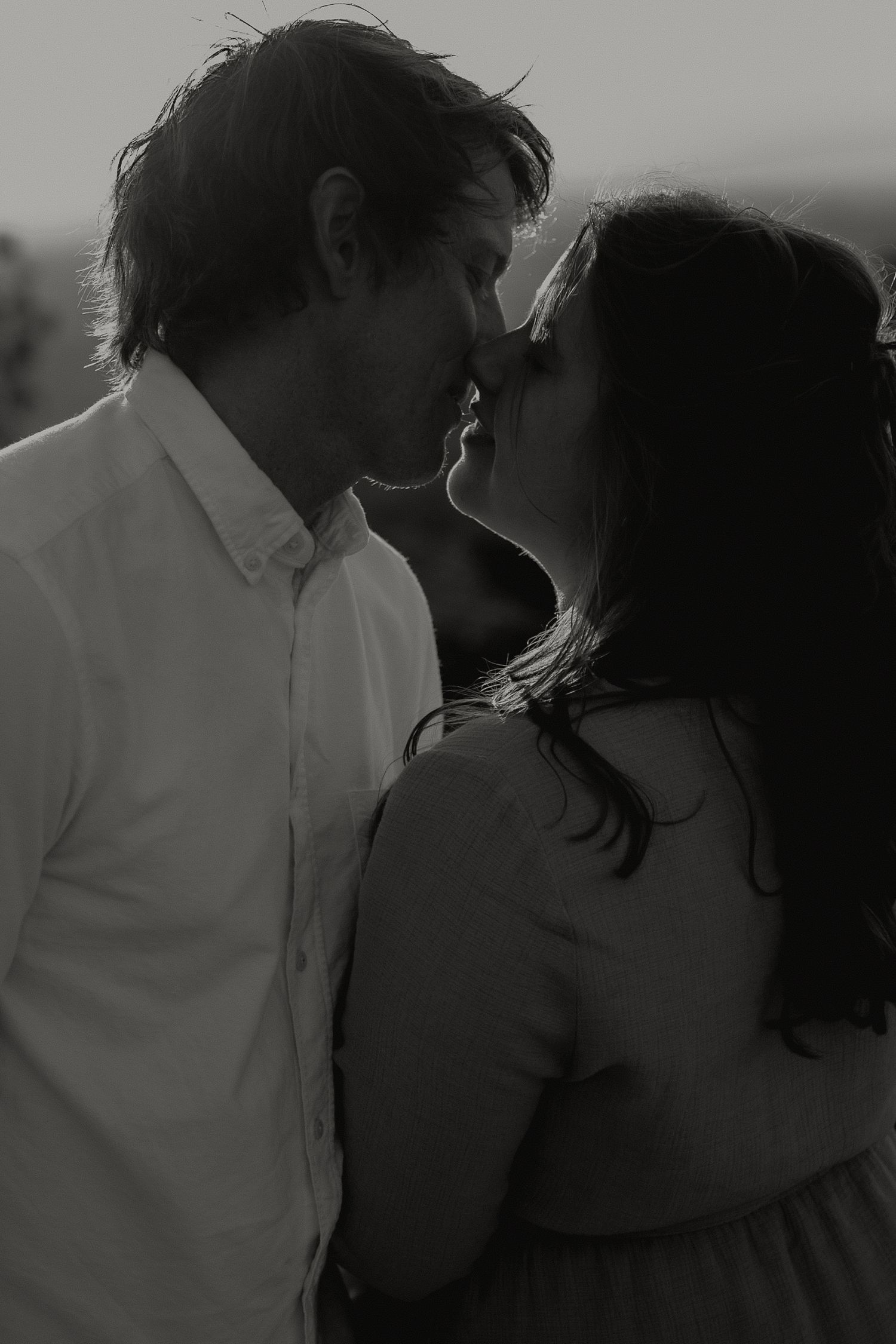 Black and white intimate close-up of couple sharing a kiss at sunset outdoors.