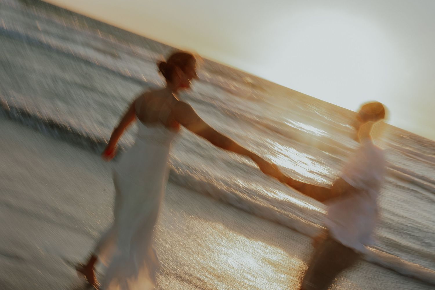 Motion-blurred romantic couple running hand in hand along glowing sunset beach shoreline.