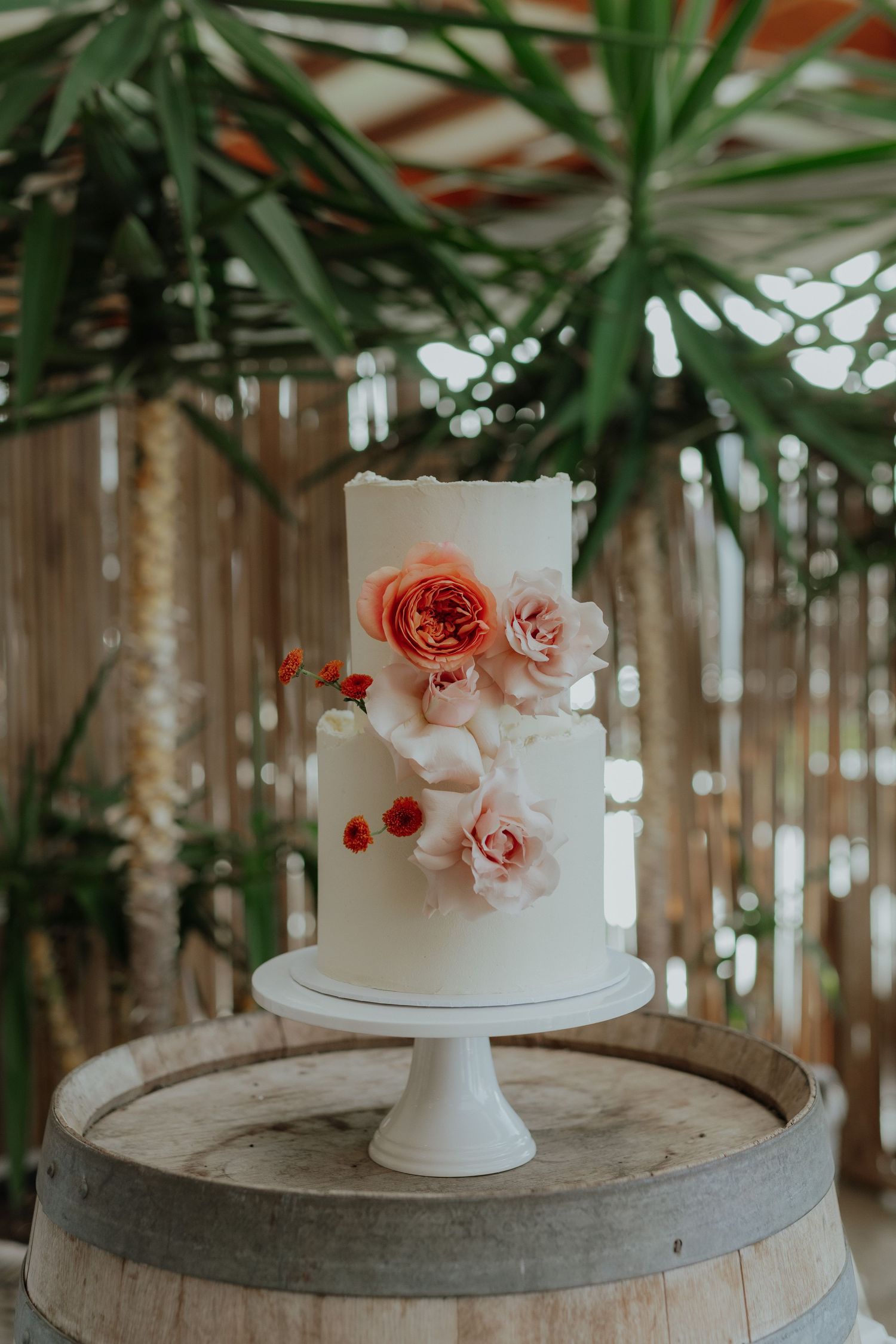 Elegant two-tier white wedding cake with pink roses on a barrel.