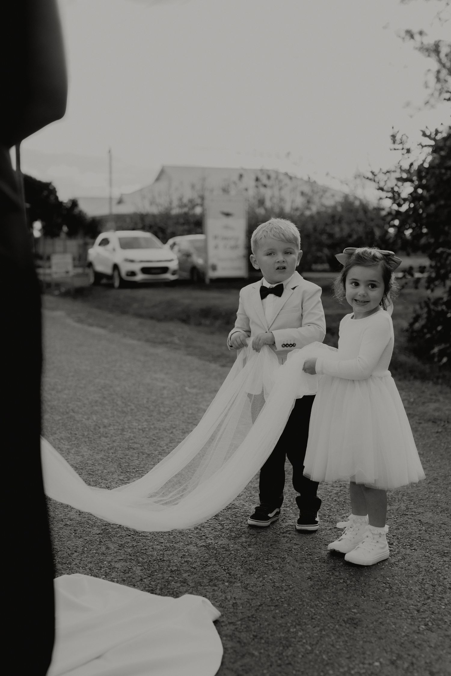 Young ring bearer and flower girl hold bride's train in black and white wedding photo.