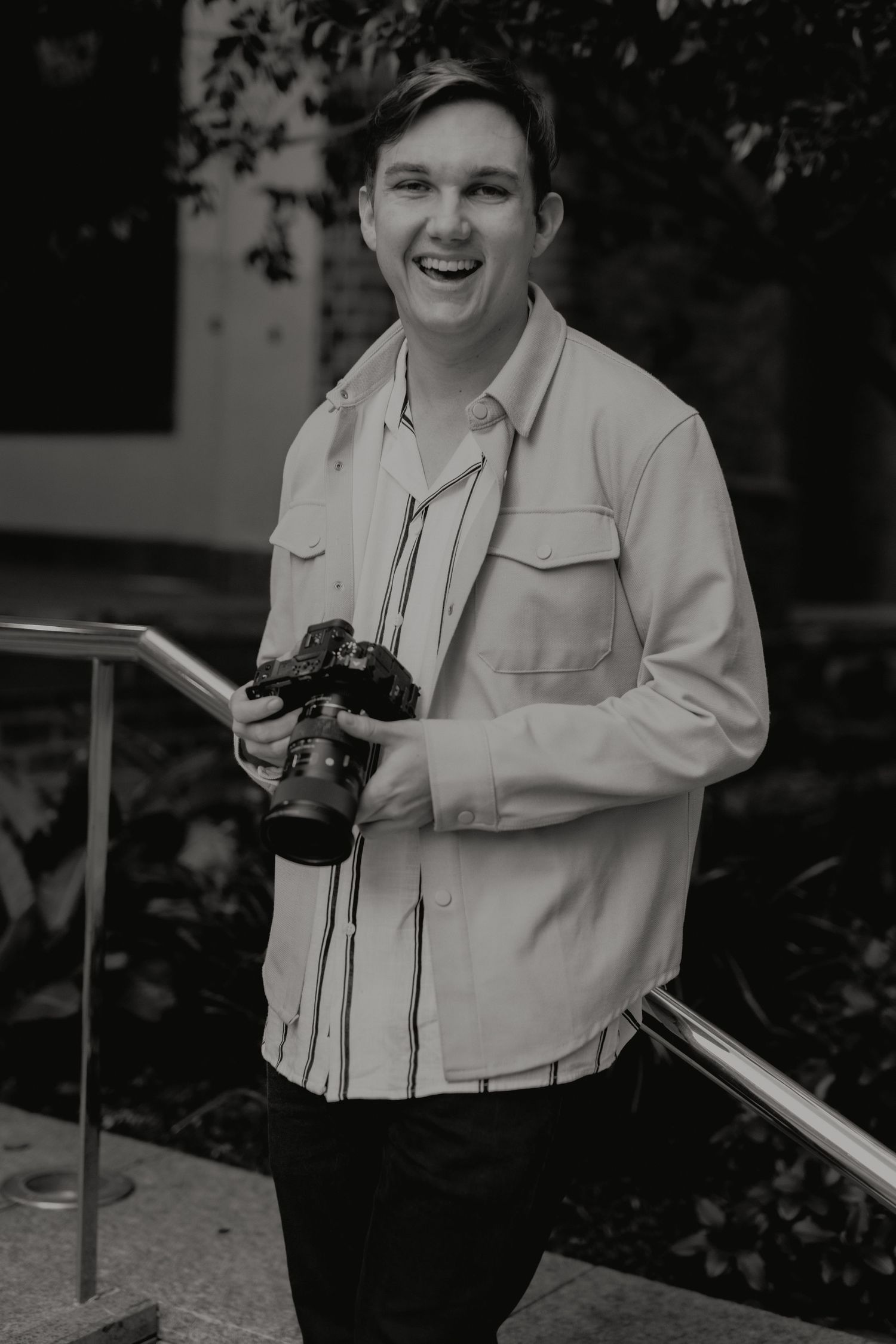 Laughing young man holding camera on outdoor staircase in black and white photography.