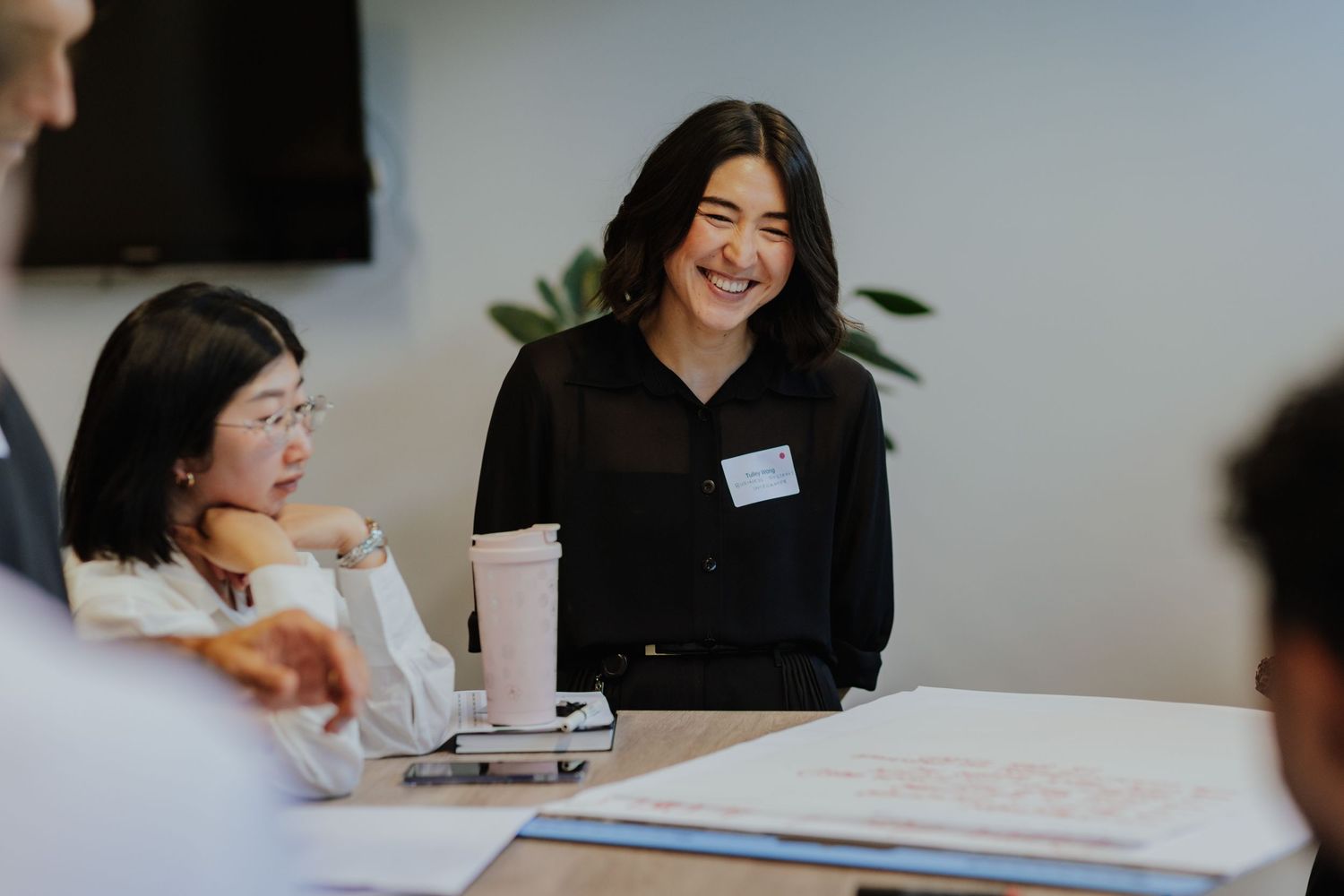 Smiling young Asian woman in black top with name tag at a business meeting table.
