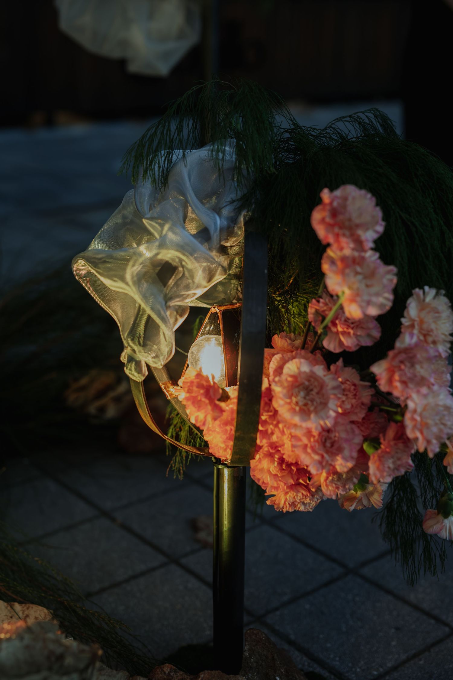 Elegant floral arrangement with pink carnations and a glowing lantern with smoke at a nighttime event.