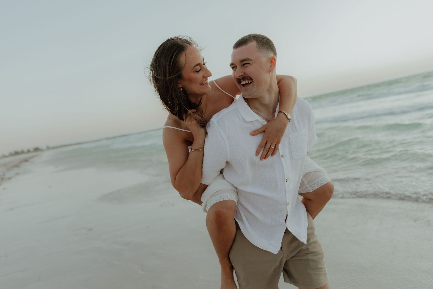 Joyful couple laughing together on a turquoise beach, woman riding piggyback.