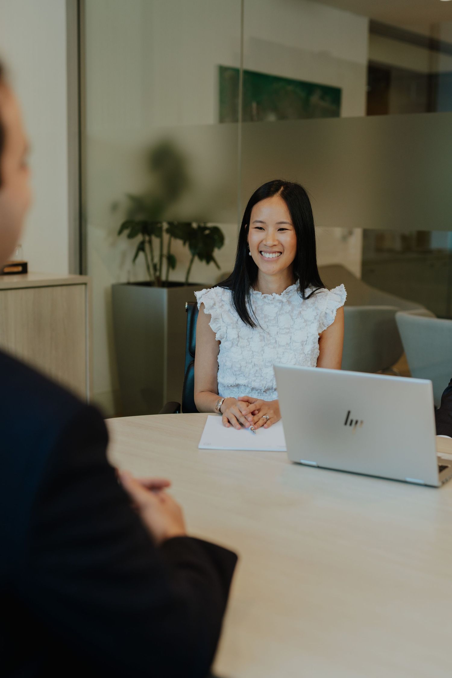Smiling Asian businesswoman in light blue top seated at conference table during office meeting.
