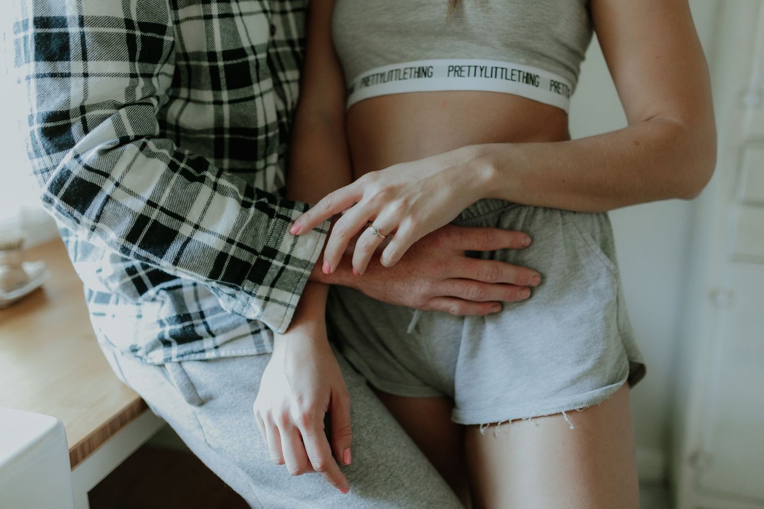 Close-up of couple embracing indoors, woman wearing PrettyLittleThing crop top and shorts with engagement ring visible.