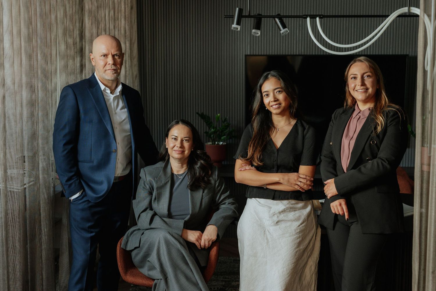 Diverse team of four business professionals posing together in a stylish modern office setting.