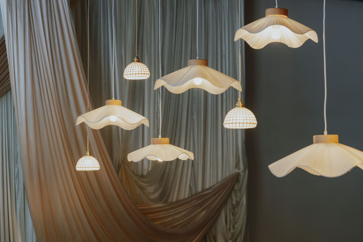 Cluster of decorative wavy white pendant lights hanging against sheer draped curtains in an event venue.