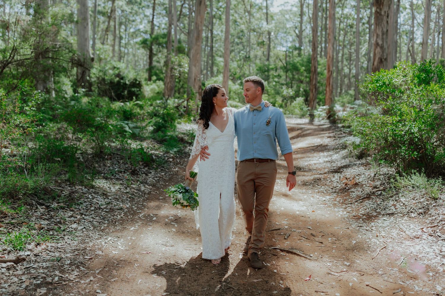 Bride and groom walk hand in hand along a scenic forest trail on their wedding day.