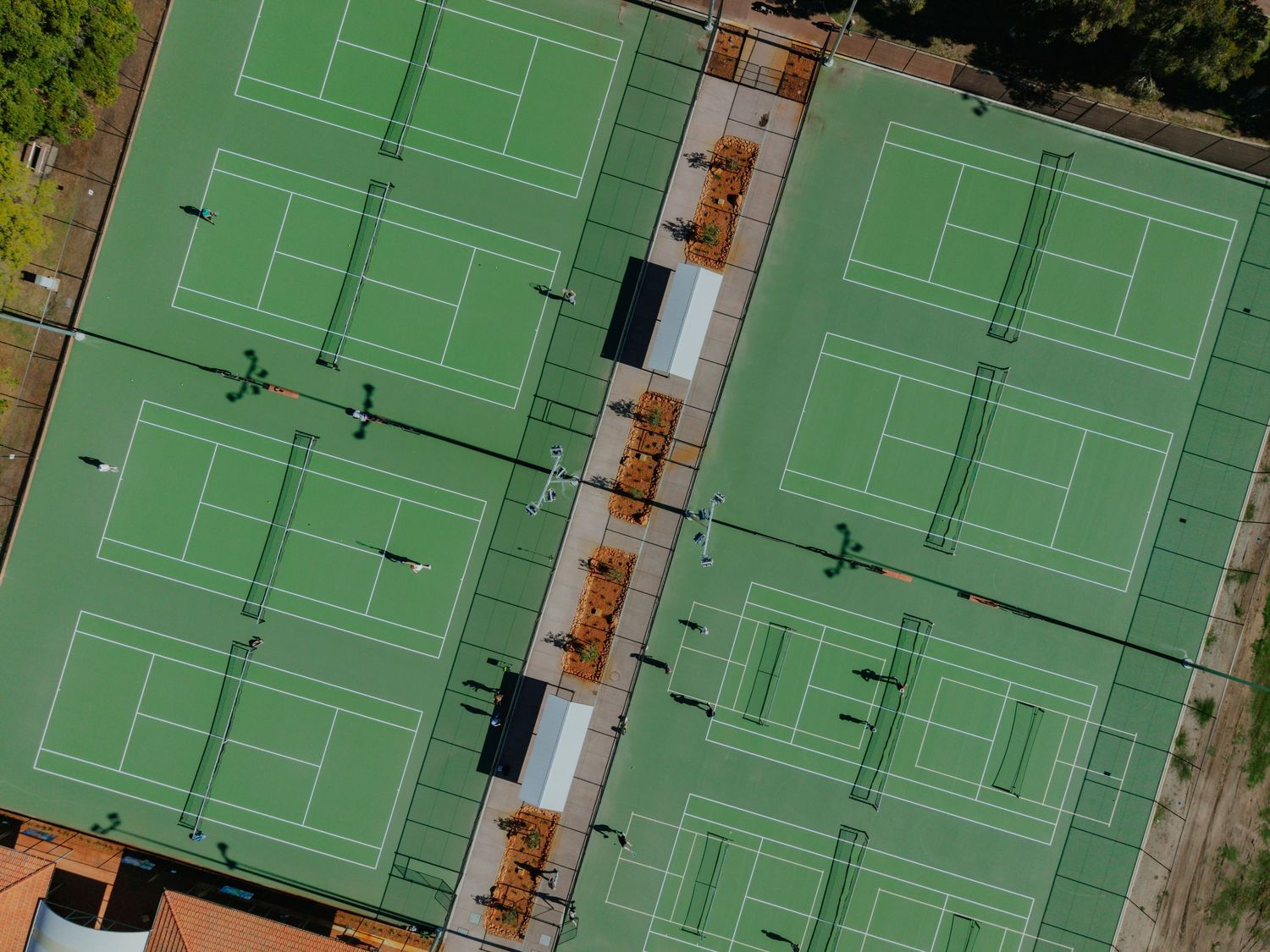 Aerial drone view of multiple green tennis courts with orange equipment between them.