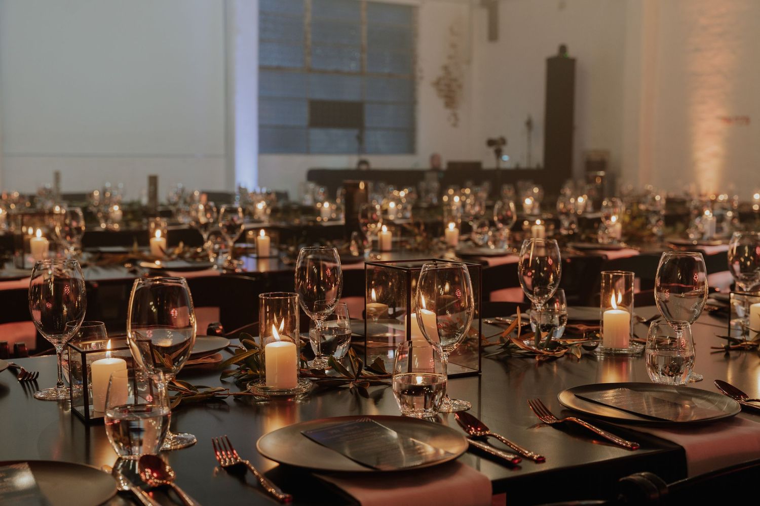 Elegant event venue with candlelit tables, crystal glassware, and dark moody reception decor.