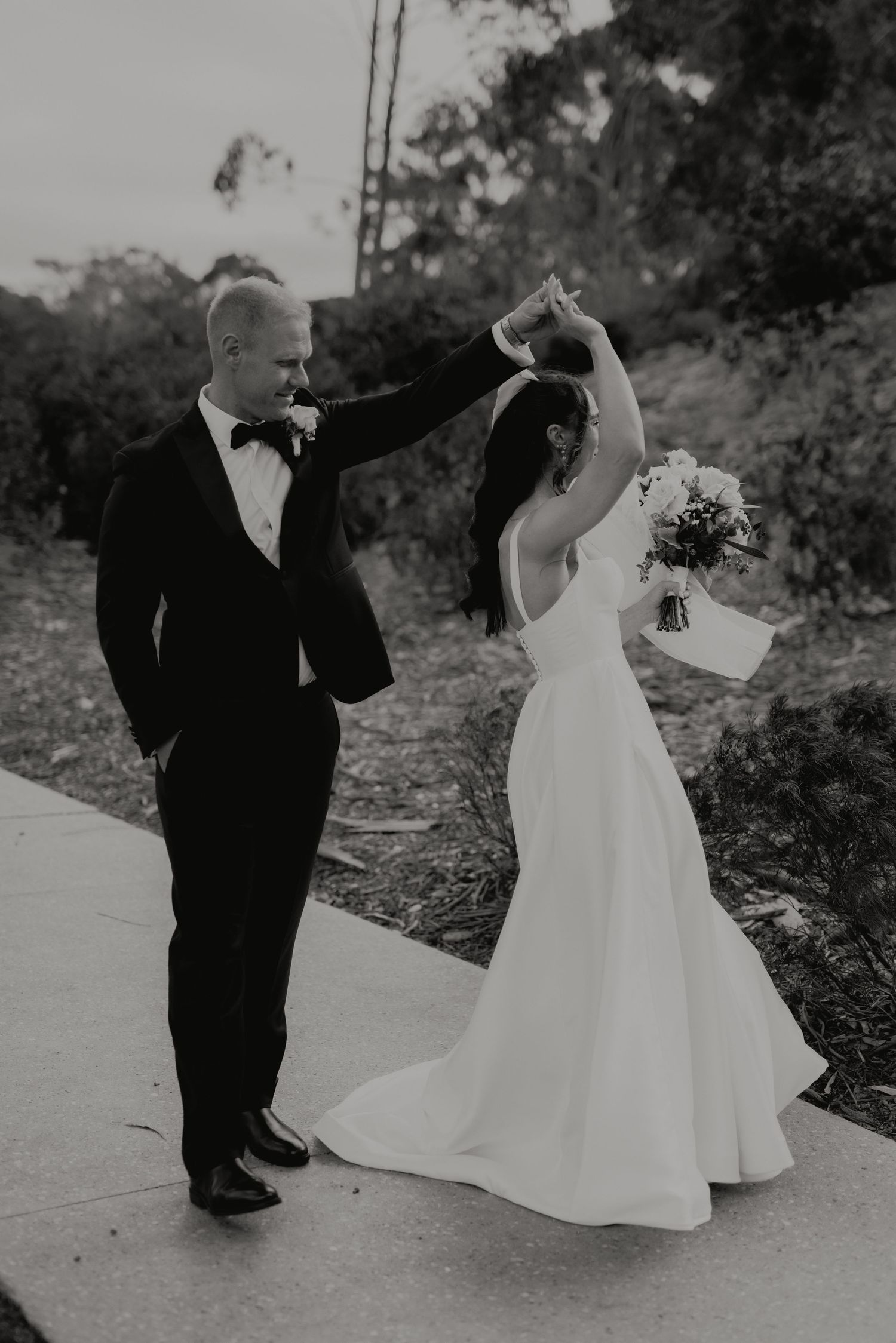 Groom twirls bride in wedding dress outdoors in black and white romantic wedding photo.