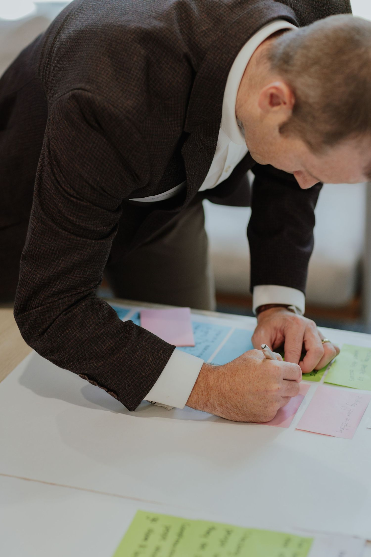 Businessman in dark suit writing on colorful sticky notes on a white table.