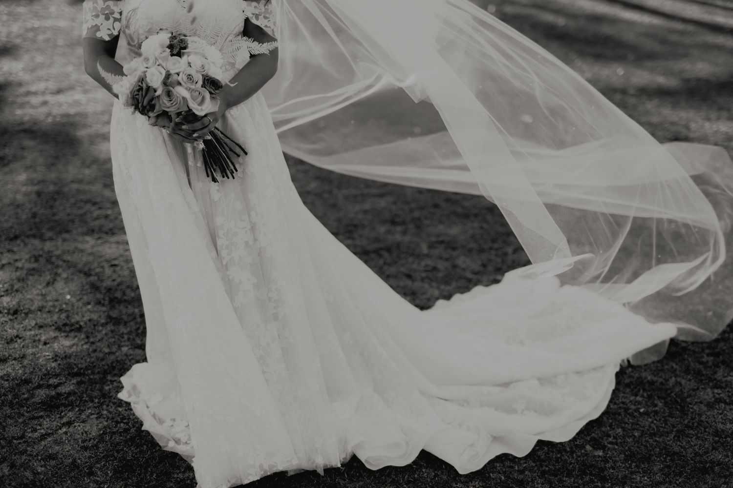 Black and white photo of bride holding bouquet with flowing veil dramatically billowing in the wind.