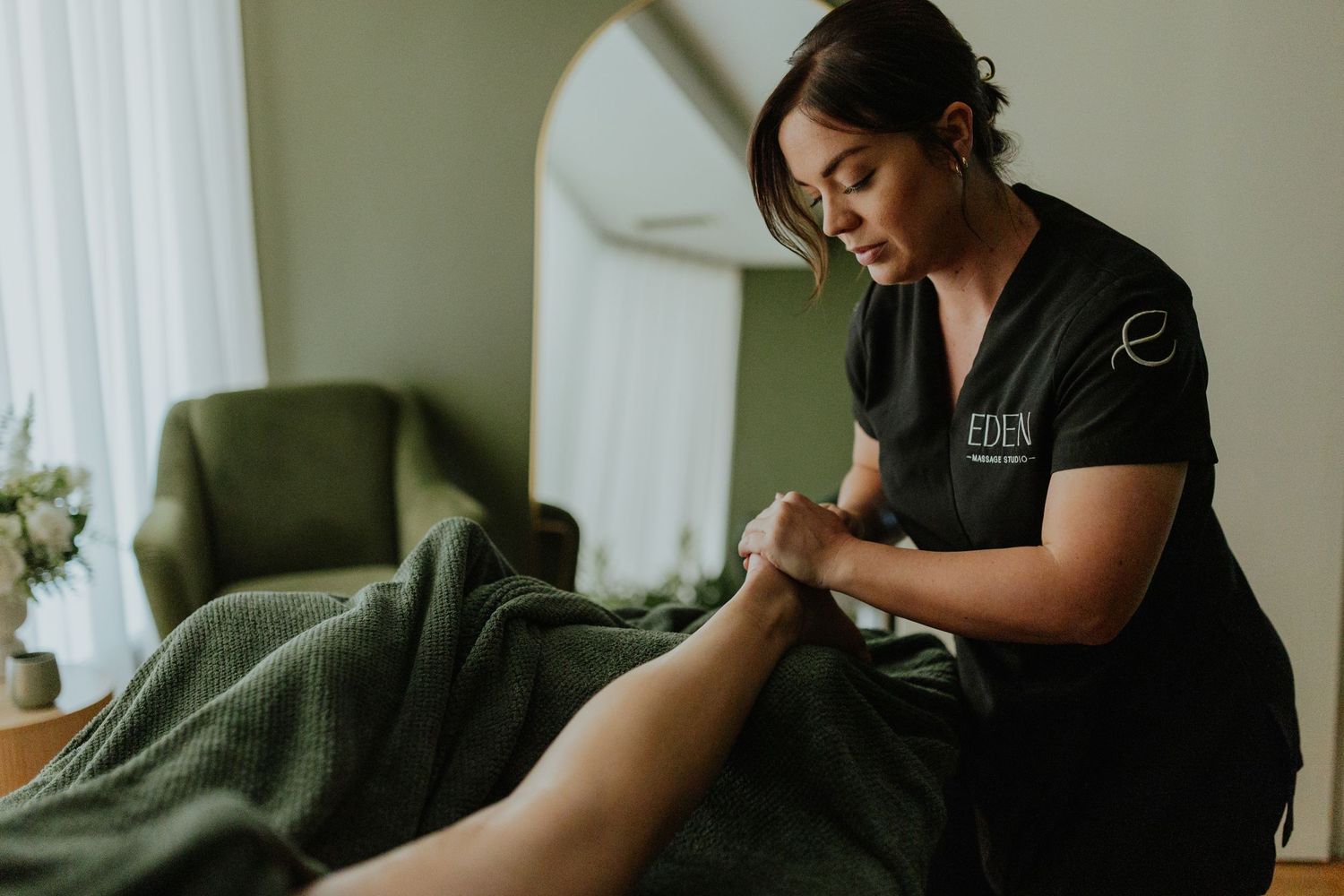 Eden Massage Studio therapist in black uniform performing a relaxing foot and leg massage on a client.