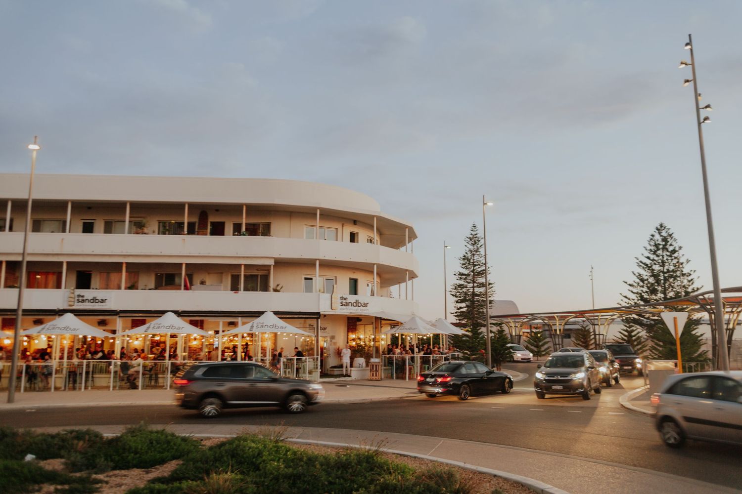 Beachside restaurant with outdoor seating and white umbrellas at dusk near the ocean.