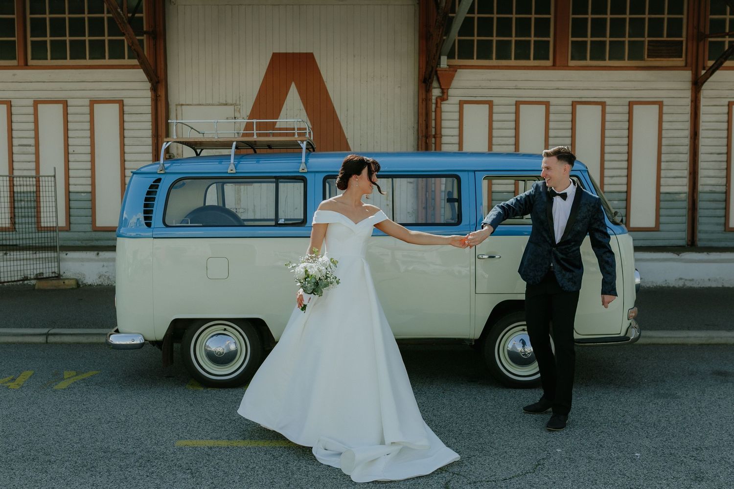 Bride and groom pose beside a vintage blue VW bus at wedding.