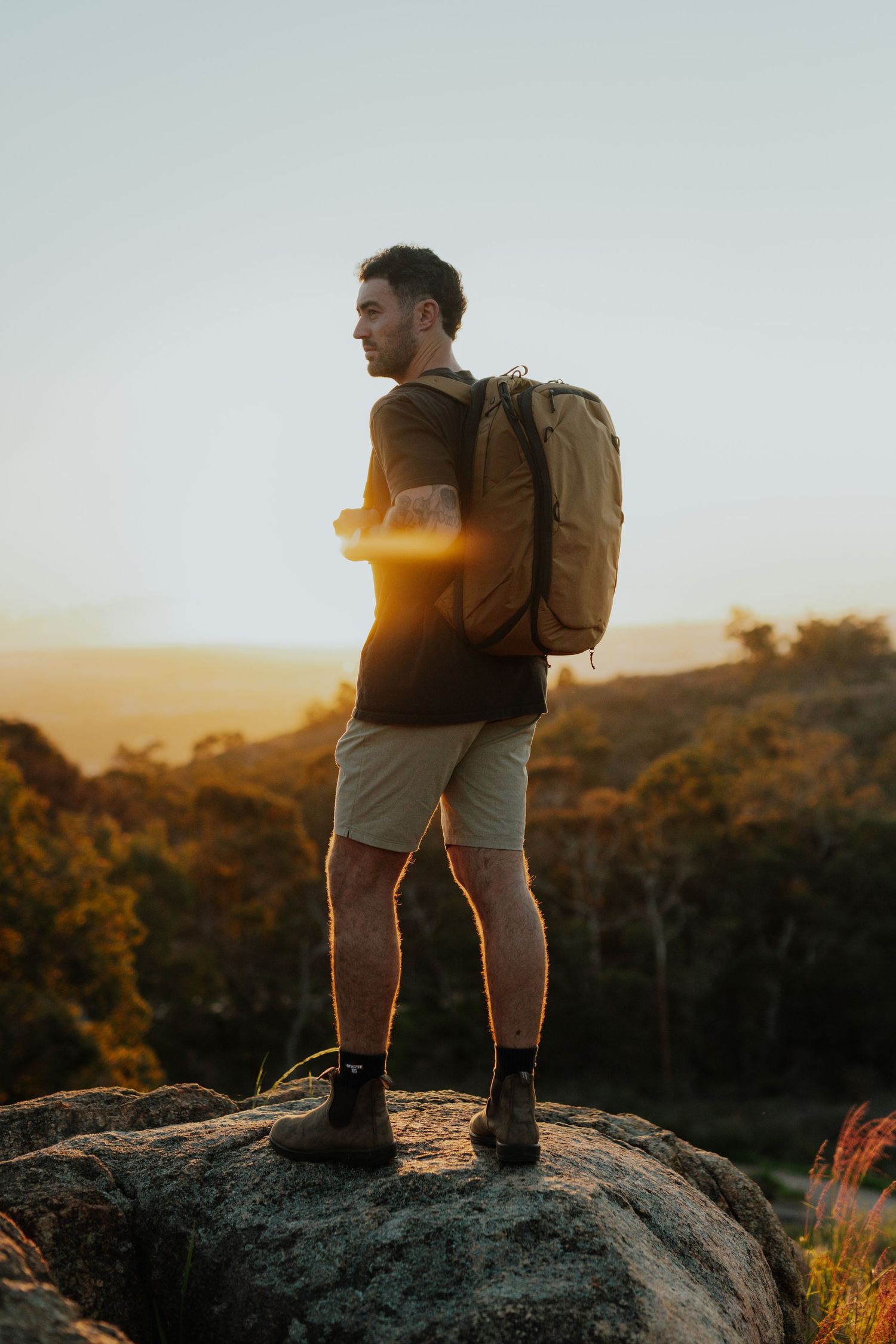 Man with backpack standing on rock at sunset overlooking forested valley.