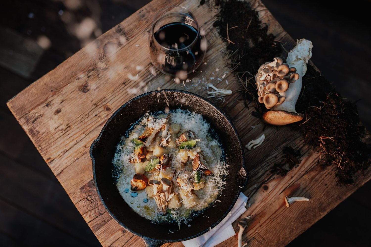 Rustic cast iron skillet with creamy mushroom dish on a wooden board with herbs.