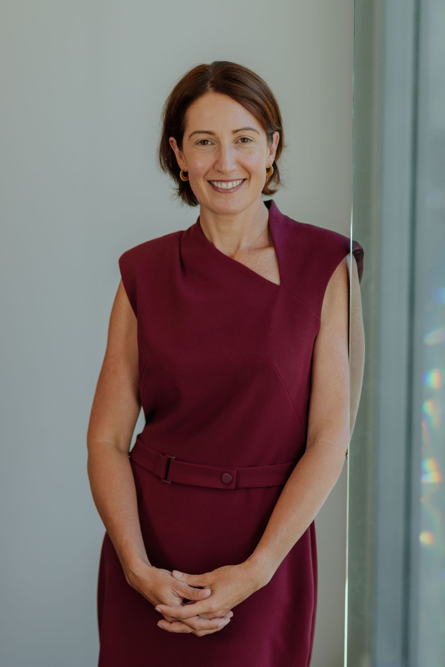 Smiling professional woman in a burgundy sleeveless dress standing confidently in a modern office.