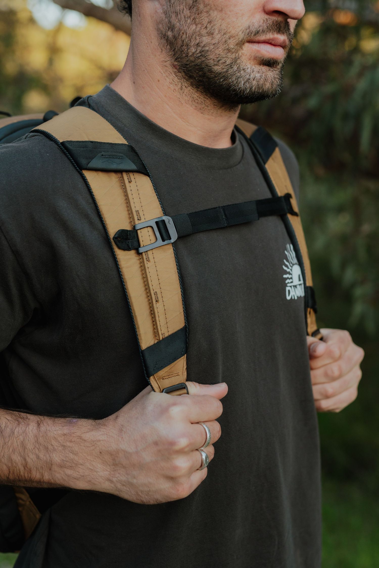 Close-up of man wearing tan and black hiking backpack with chest strap outdoors.