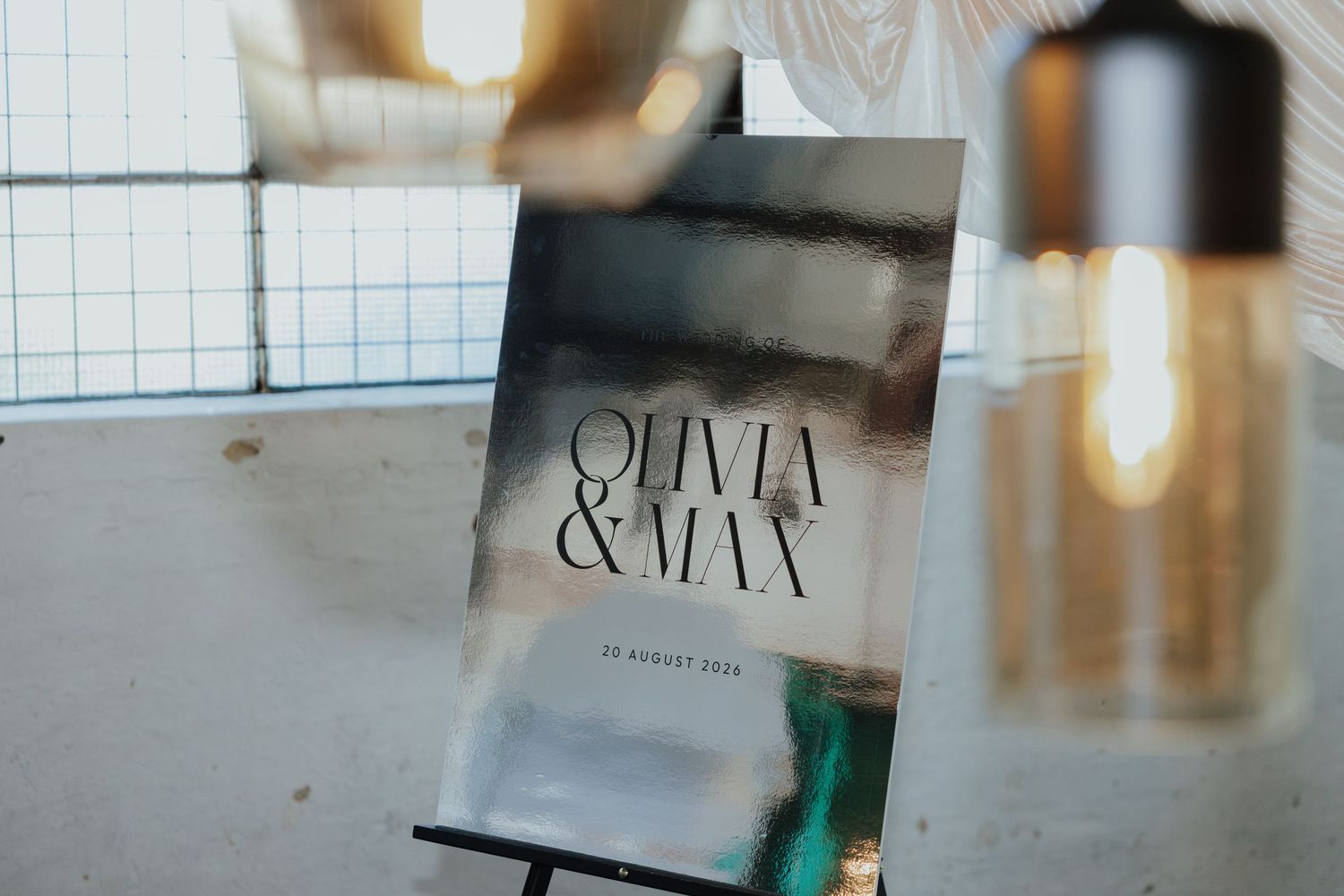 Wedding welcome sign for Olivia and Max on an easel with warm pendant light in the foreground.