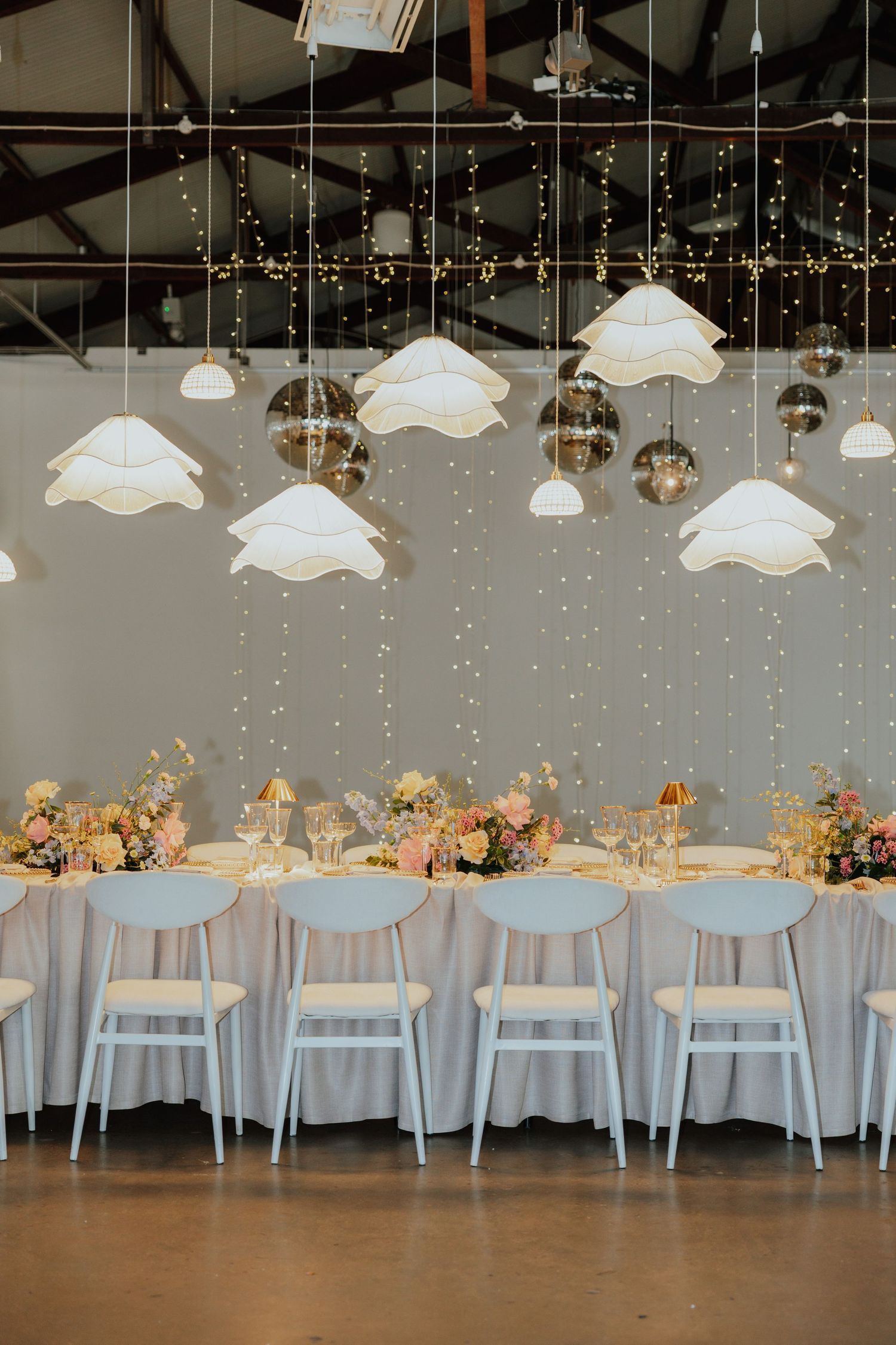 Elegant wedding reception table set with flowers under white cloud pendants and mirrored disco balls.